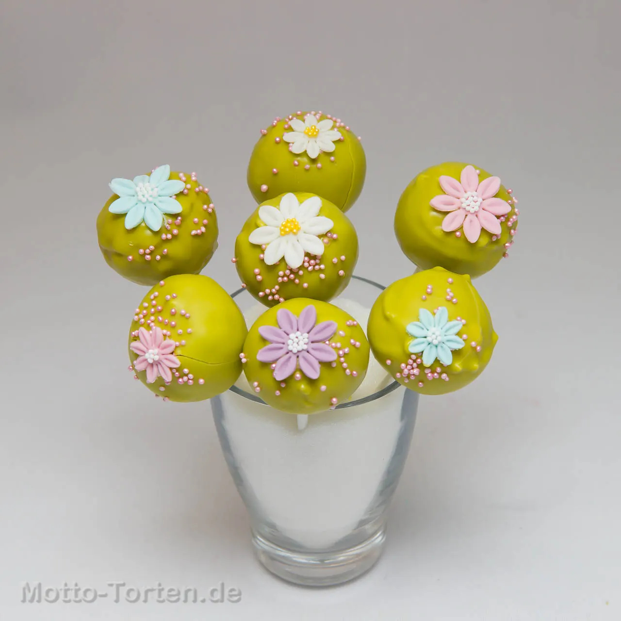 Cakepops in Limettengrün mit pastellfarbenen Zuckerblüten und rosa Perlen