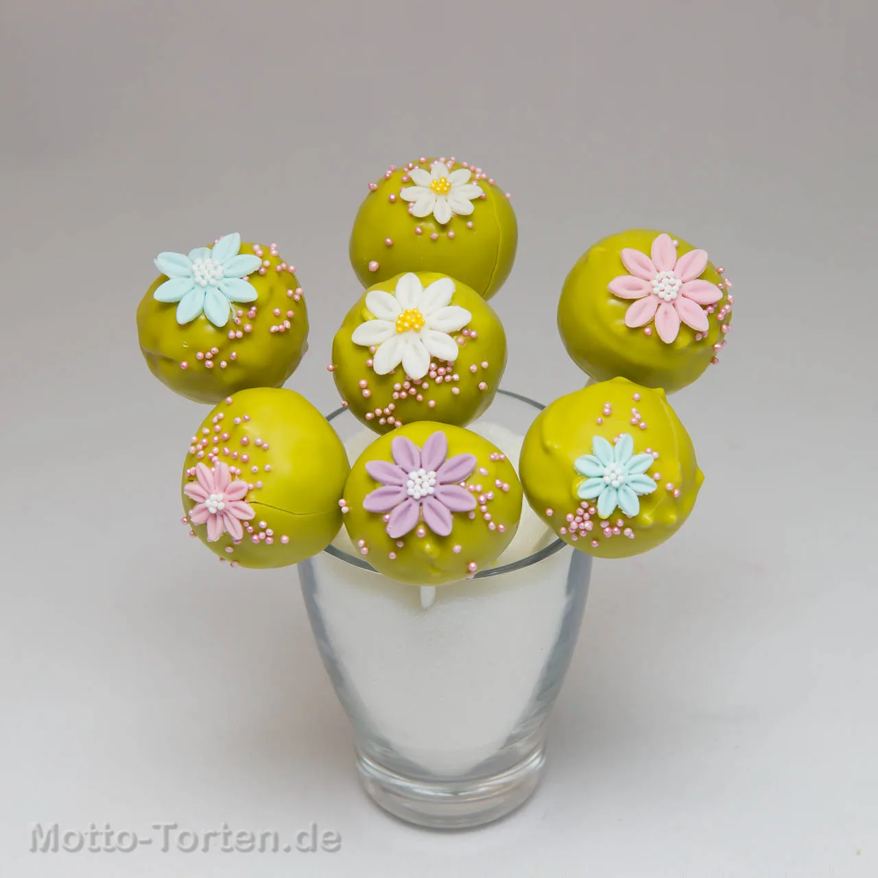 Cakepops in Limettengrün mit pastellfarbenen Zuckerblüten und rosa Perlen