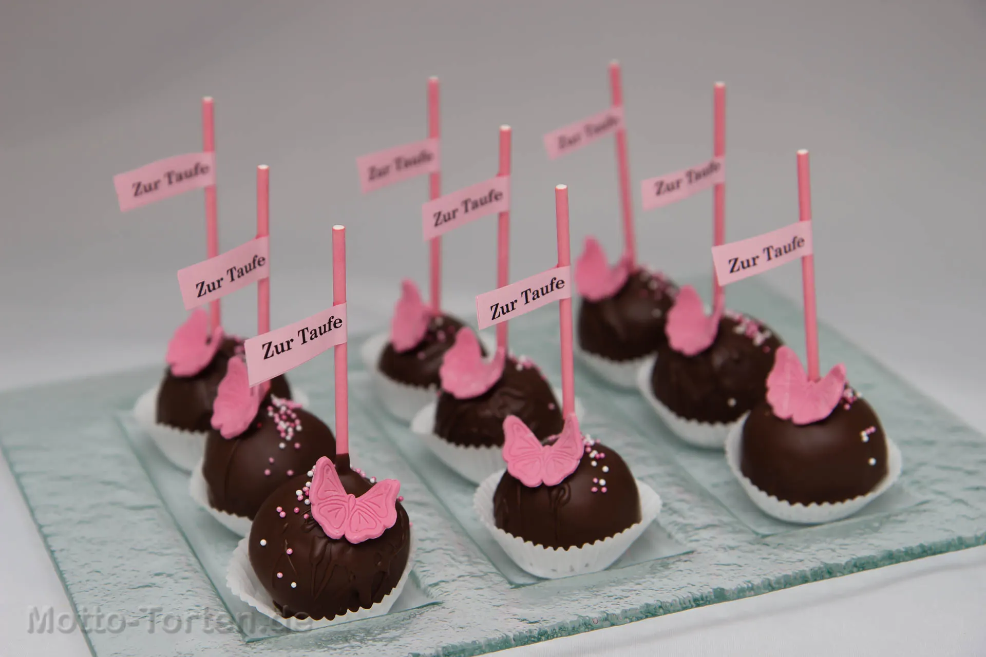 Schokoladen-Cakepops mit rosa Schmetterlingen und Fähnchen mit der Aufschrift „Zur Taufe“