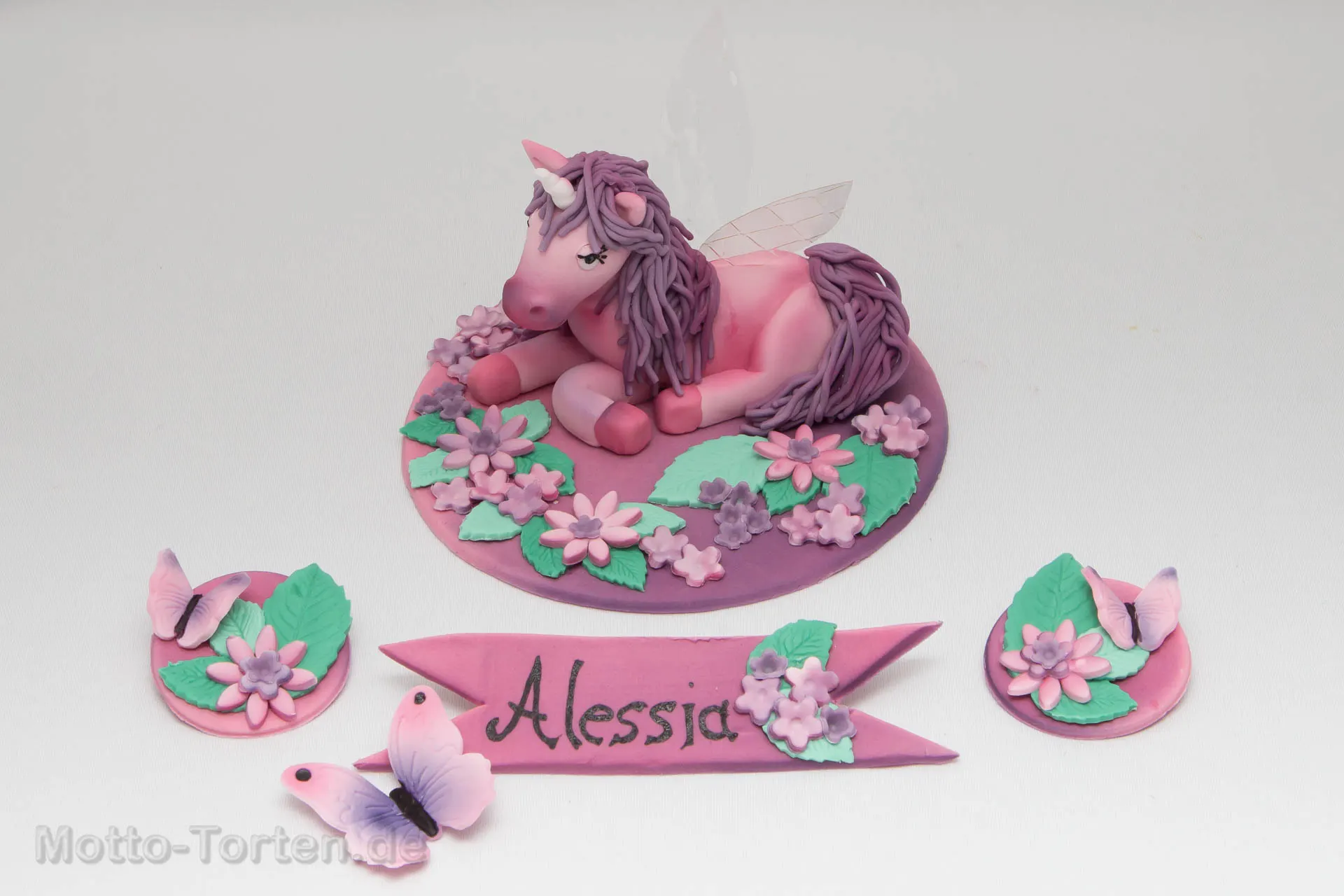 Handmodelliertes rosa Einhorn aus Fondant mit Flügeln aus Gelatine, auf einer Bodenplatte mit Blumen und Namensschild