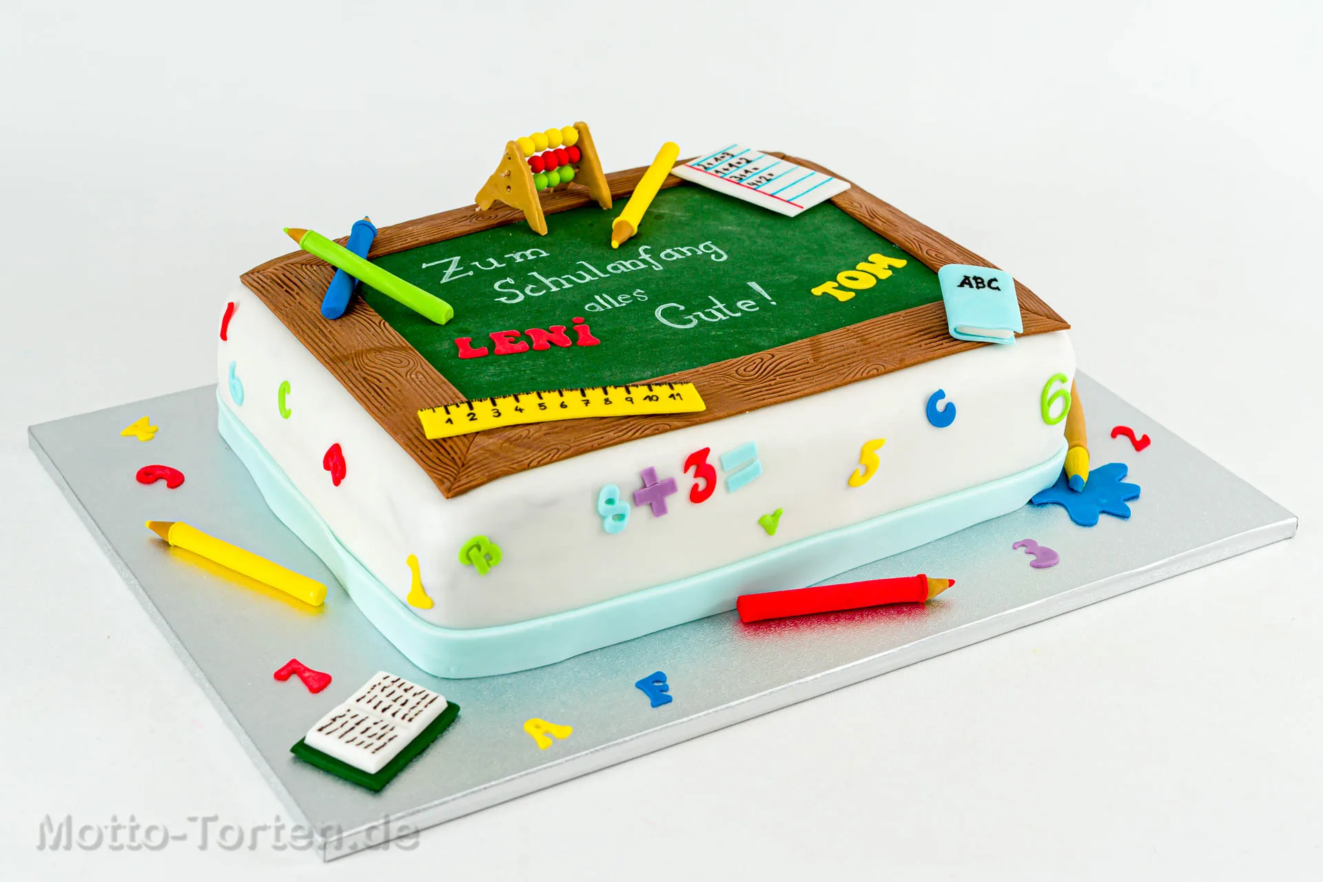 Rechteckige Einschulungstorte mit grüner Schultafel aus Fondant, Holzrahmen, Rechenschieber und bunten Buchstaben und Zahlen