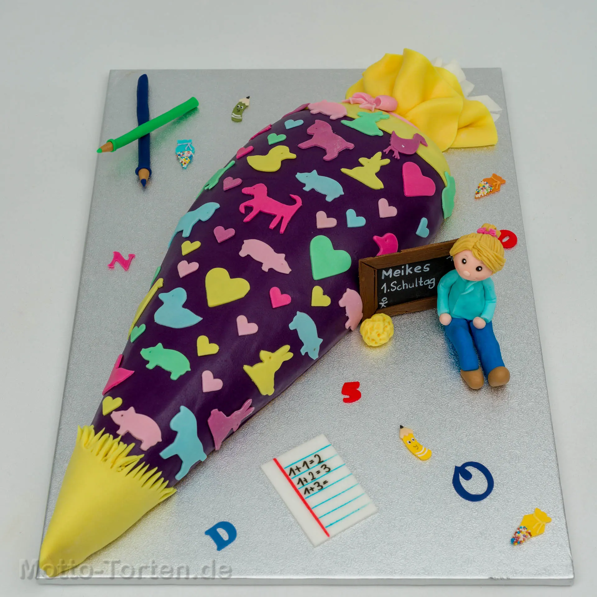 Schultüte als Torte in Violett mit bunten Tierfiguren und Herzen, dazu eine modellierte Schulanfängerin an einer Tafel