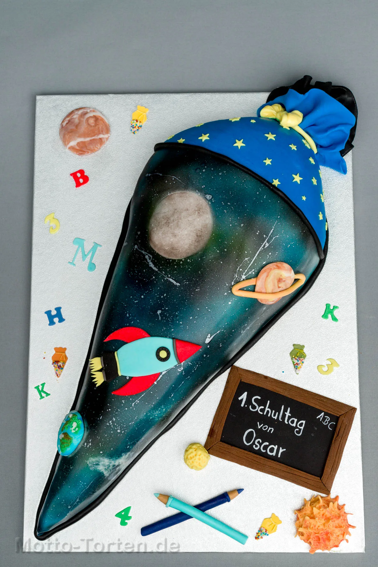 Schultüte als Torte mit aufgesprühtem Sternenhimmel, Planeten und einer Rakete aus Fondant