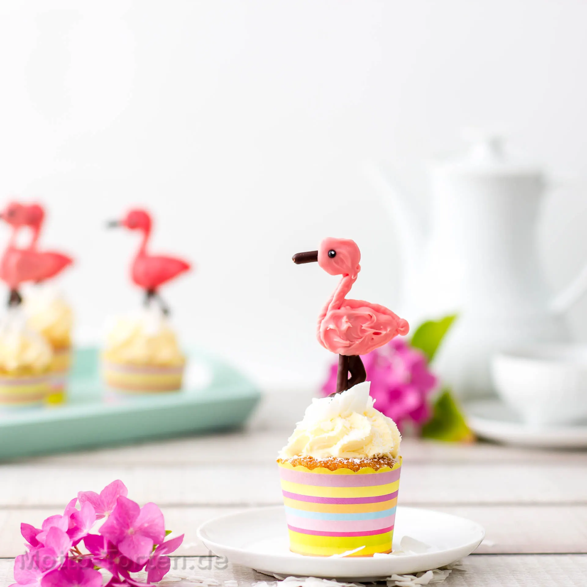 Cupcake mit Kokosbuttercreme und Kokosraspeln, darauf ein Flamingo aus rosa Schokolade mit Beinen und Schnabel aus dunkler Schokolade