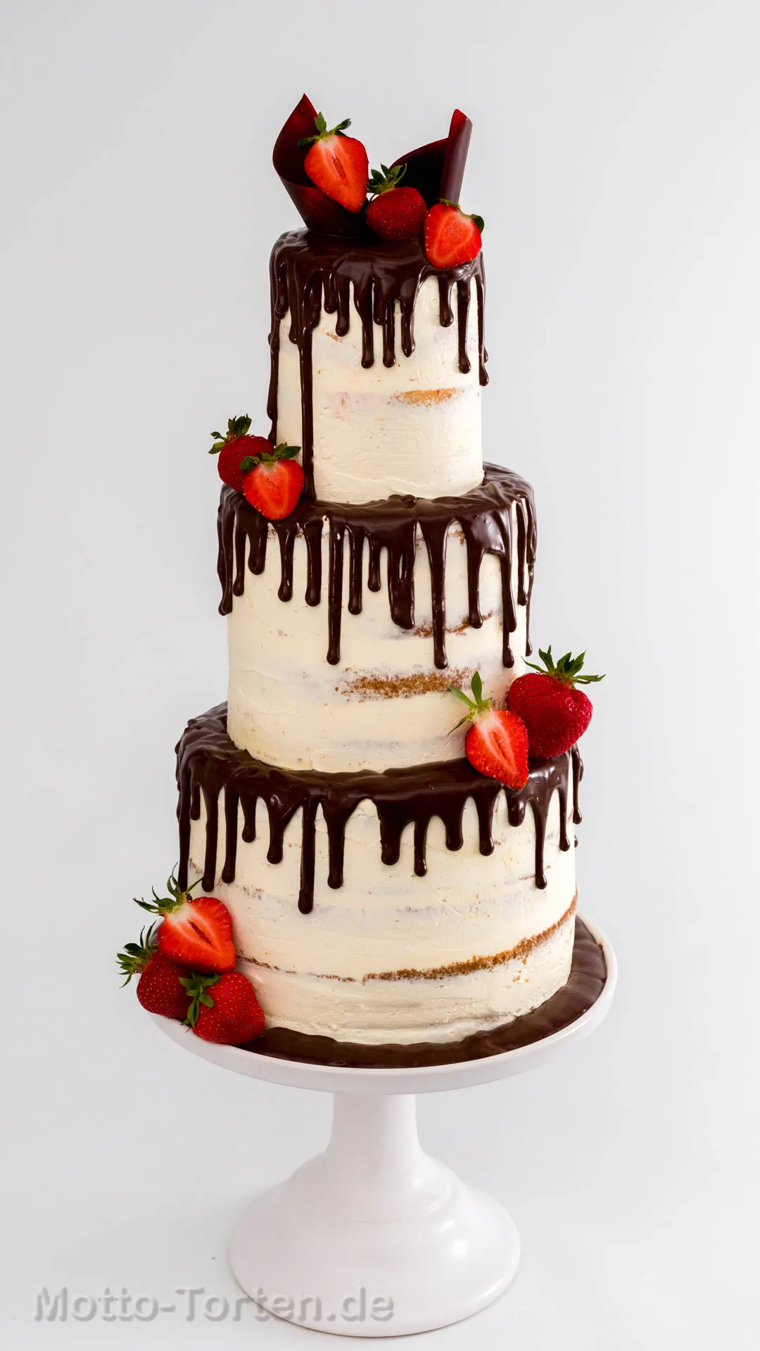 Dreistöckige Torte in heller Buttercreme mit dunklem Schokoladen-Drip, frischen Erdbeeren und Kuvertüreornamenten, auf einem weißen Tortenständer