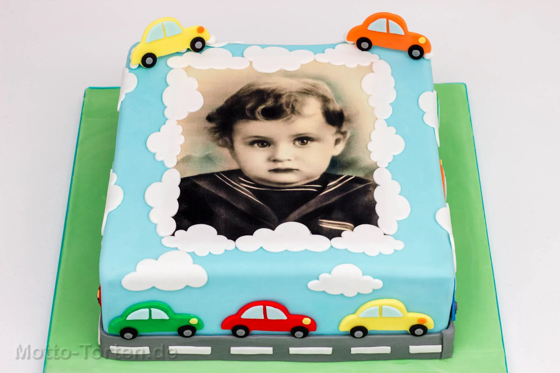 Geburtstagstorte mit einem aufgelegten Kinderfoto des Geburtstagskindes und bunten Spielzeugautos aus Fondant
