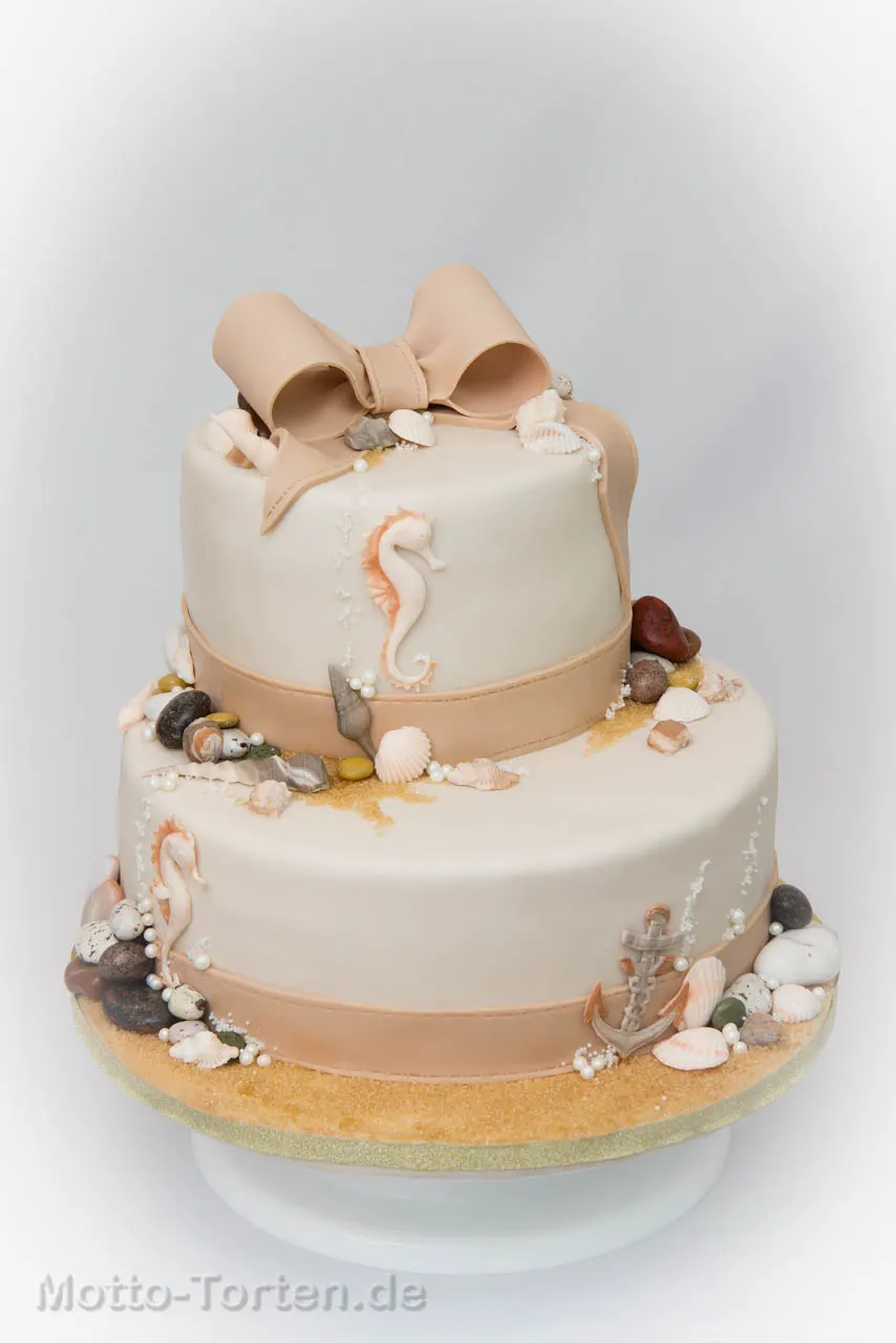 Zweistöckige Hochzeitstorte in Creme- und Nougattönen mit Muscheln, Seepferdchen, Anker und Kieseln aus Fondant, Sand aus Rohrzucker und großer Schleife