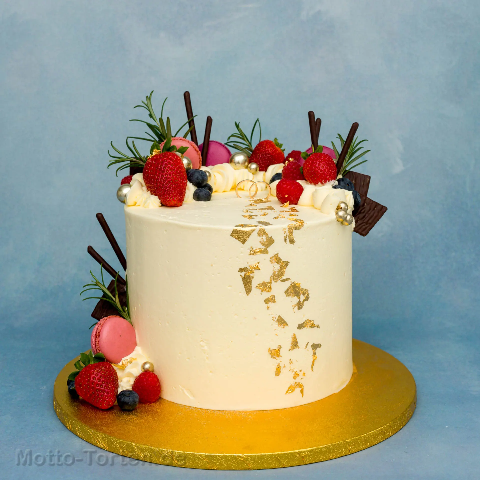 Cremefarbene Hochzeitstorte mit essbarem Blattgold, frischen Beeren und Macarons