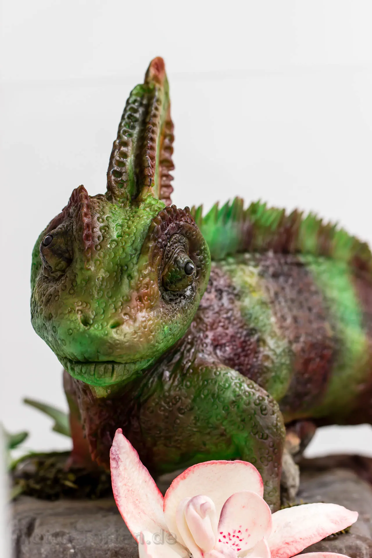 Nahaufnahme des lebensgroßen Chamäleons aus Fondant mit strukturierter Haut in Grün und Rotbraun, davor eine Orchidee aus Blütenpaste