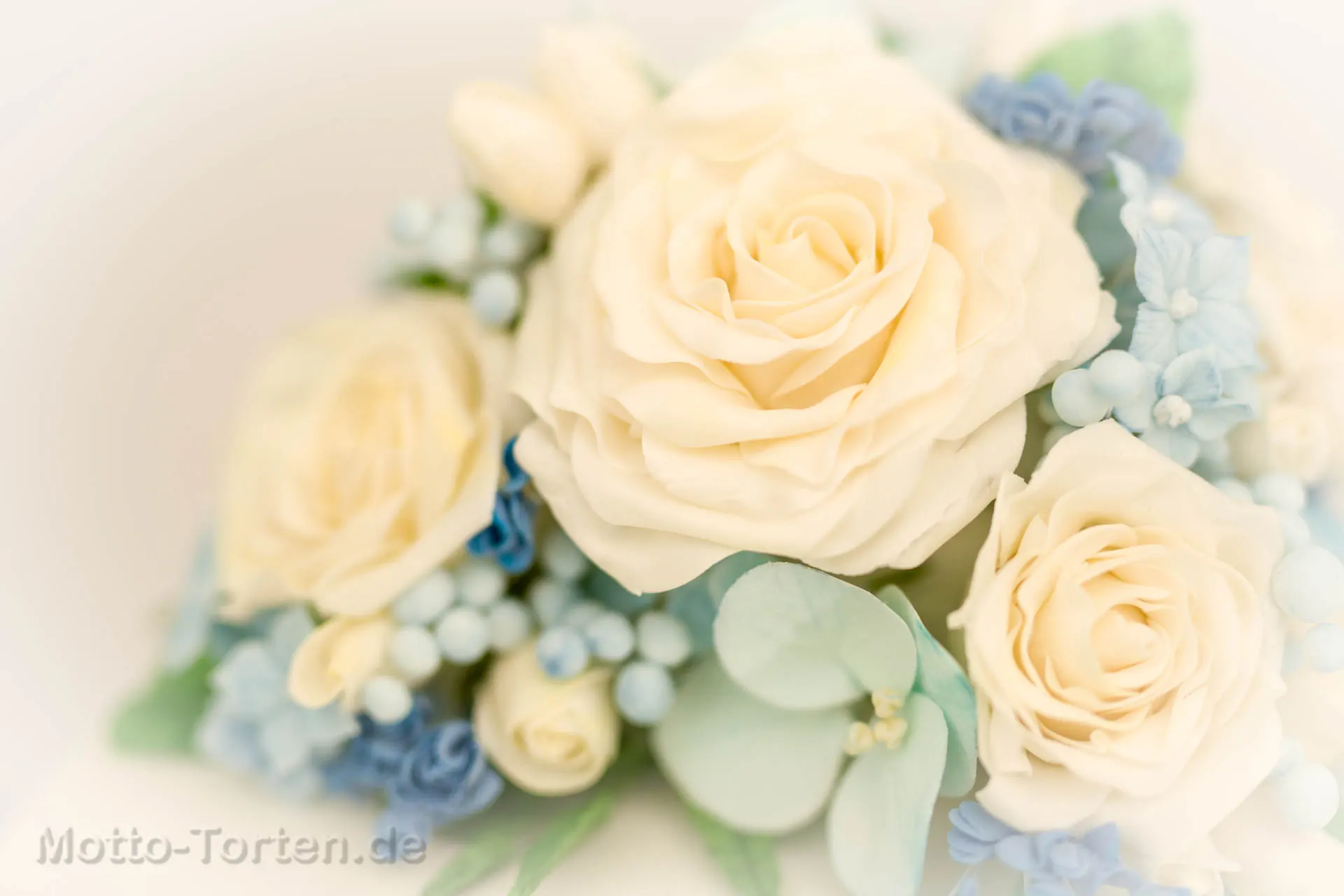 Nahaufnahme des Bouquets auf der Hochzeitstorte: cremeweiße Rosen aus Blütenpaste mit hellblauen Füllblümchen, Beeren und Eukalyptusblättern