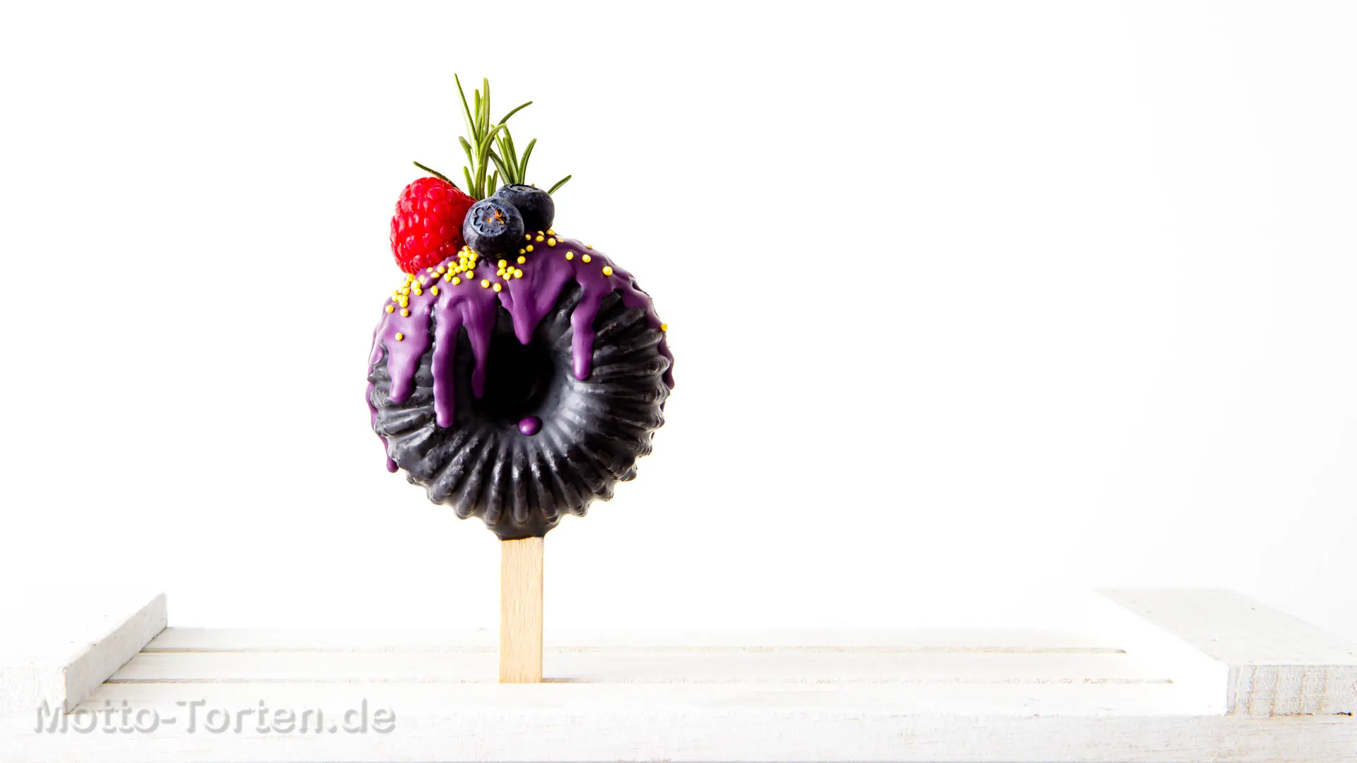 Mini-Gugelhupf am Stiel mit violetter Glasur, frischen Beeren und Rosmarin