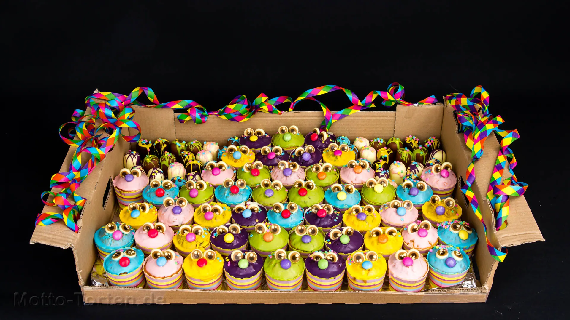 Bunte Monster-Muffins mit großen Schokoladenaugen, dekoriert mit Luftschlangen