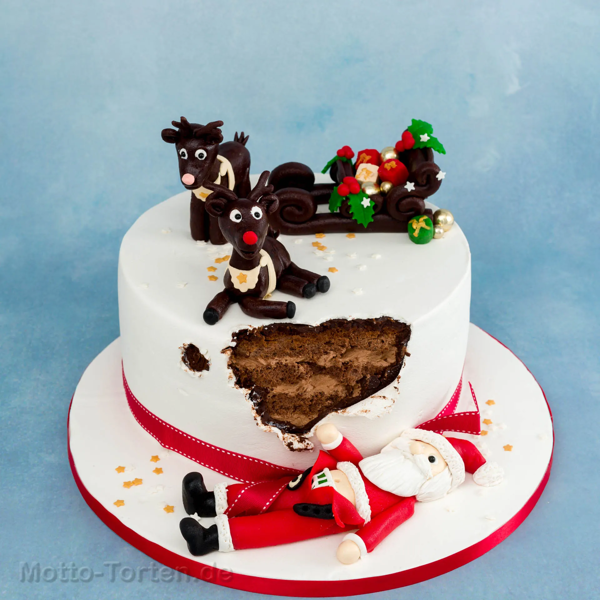 Weiße Weihnachtstorte, aus deren Wand ein modellierter Weihnachtsmann gebrochen ist, darüber Rentiere und ein Schlitten aus Fondant