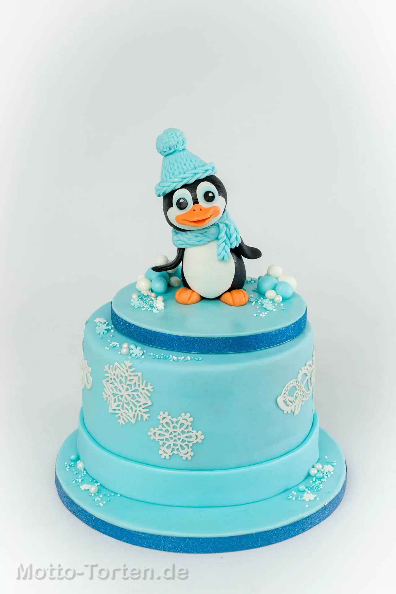 Zweistöckige babyblaue Torte mit handmodelliertem Pinguin und Schneeflocken aus essbarer Spitze
