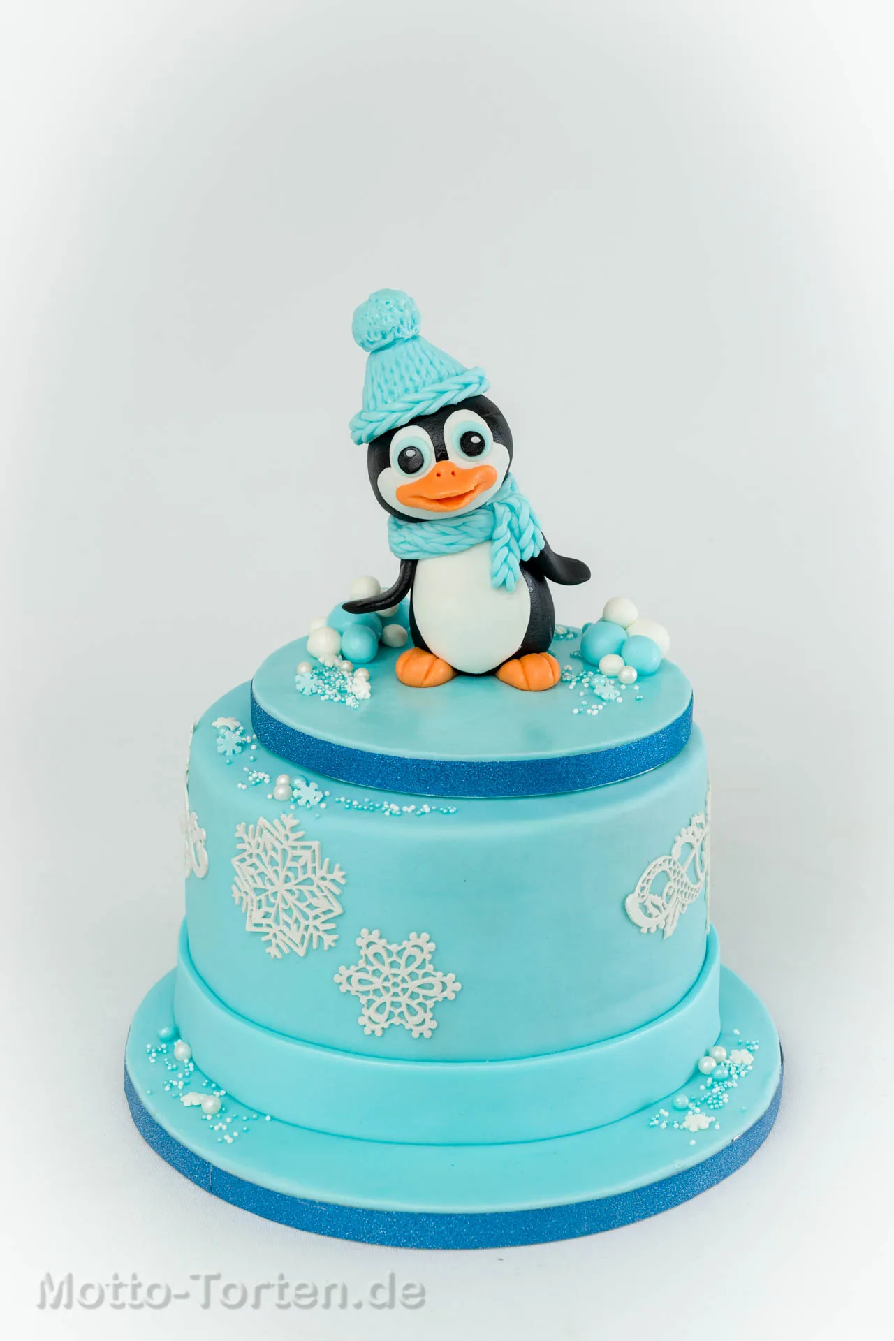 Zweistöckige babyblaue Torte mit handmodelliertem Pinguin und Schneeflocken aus essbarer Spitze