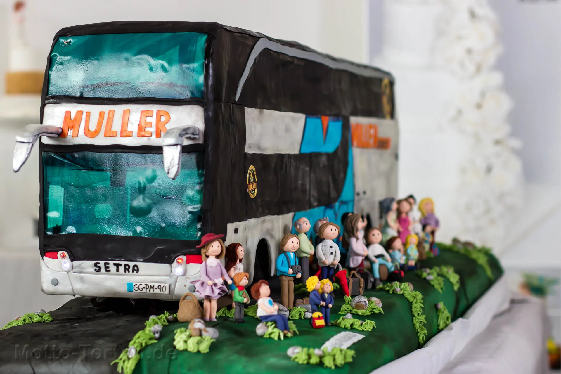 Anderthalb Meter lange Torte als Setra-Doppeldeckerbus mit Müller-Schriftzug, davor eine Reisegesellschaft aus handmodellierten Fondantfiguren mit Gepäck