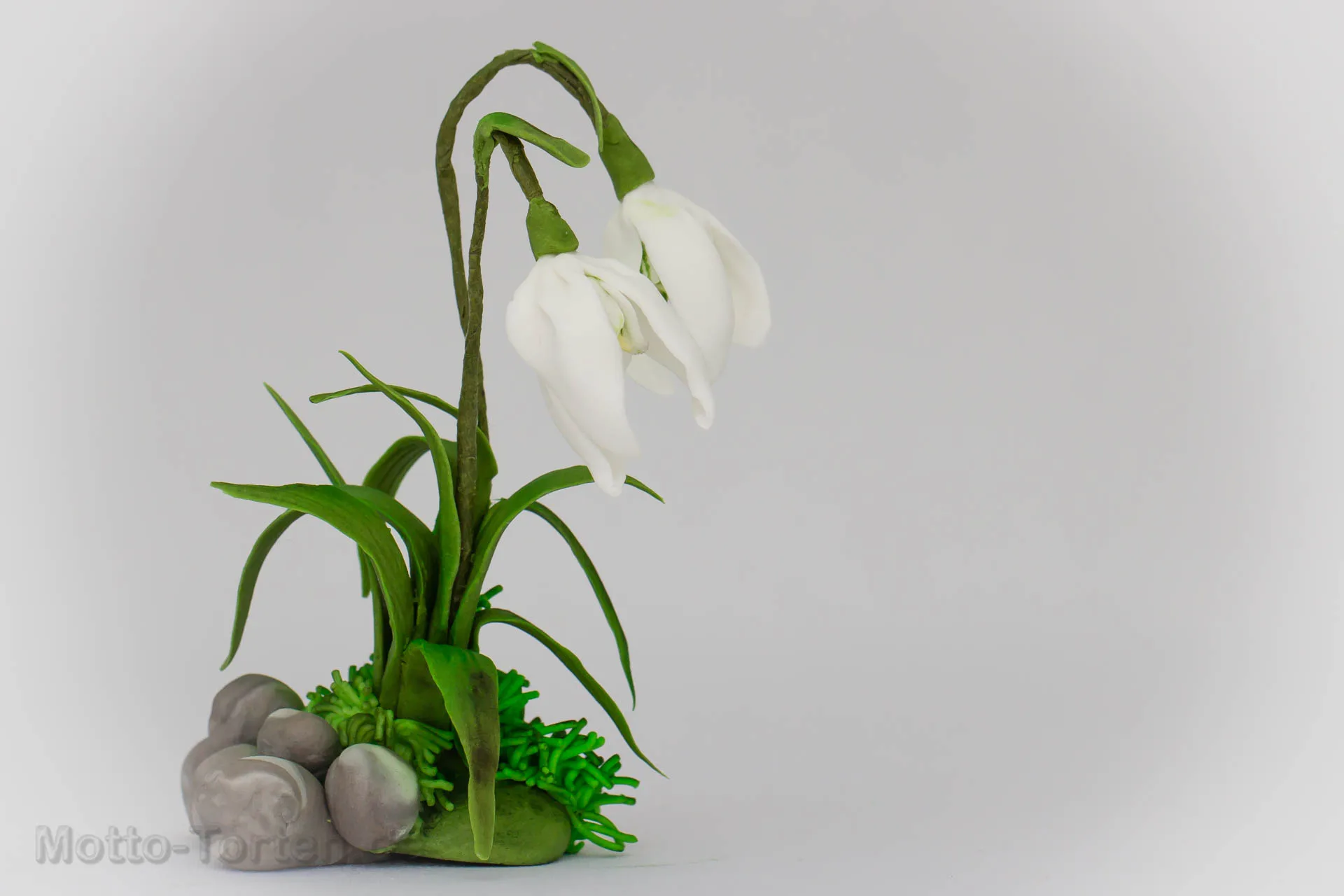 Von Hand modelliertes Schneeglöckchen aus Blütenpaste, mit grünen Blättern und Kieseln auf einem Sockel