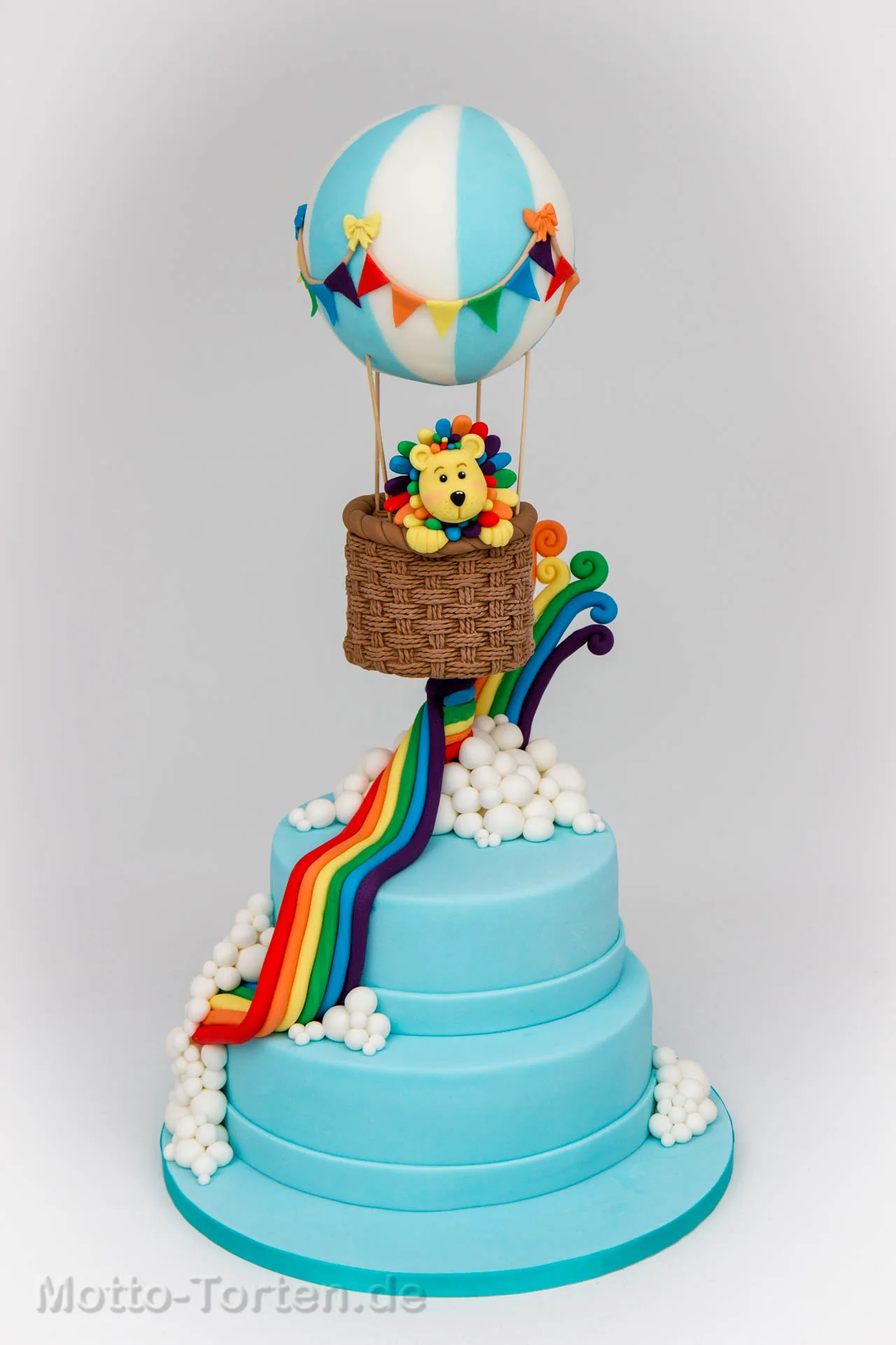 Zweistöckige Tauftorte in Hellblau mit einem Regenbogen aus Fondant und einem Löwen im Heißluftballon als Aufsatz