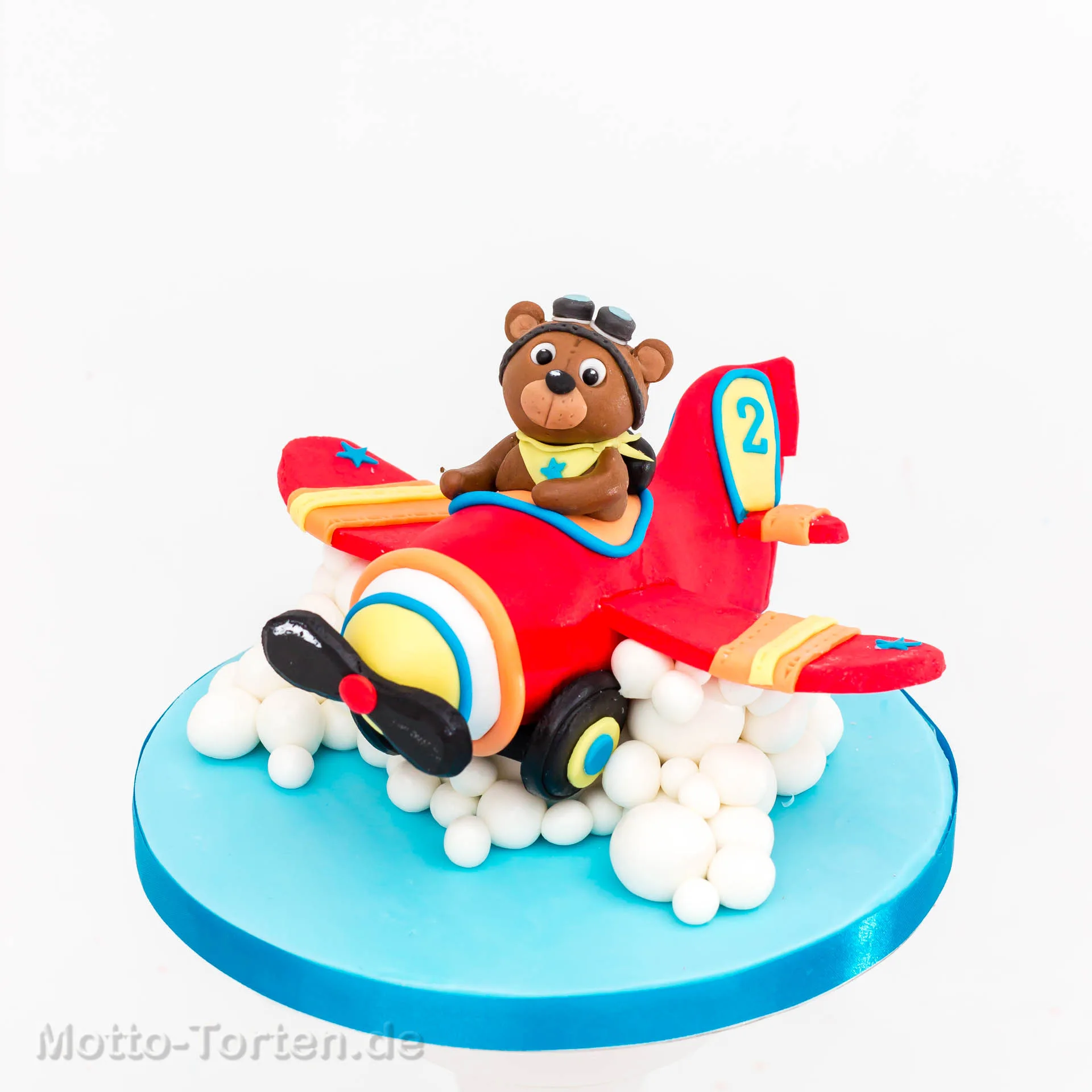 Handmodellierte Fondantfigur: Teddybär als Pilot in einem roten Flugzeug, auf einer blauen Torte mit Wolken