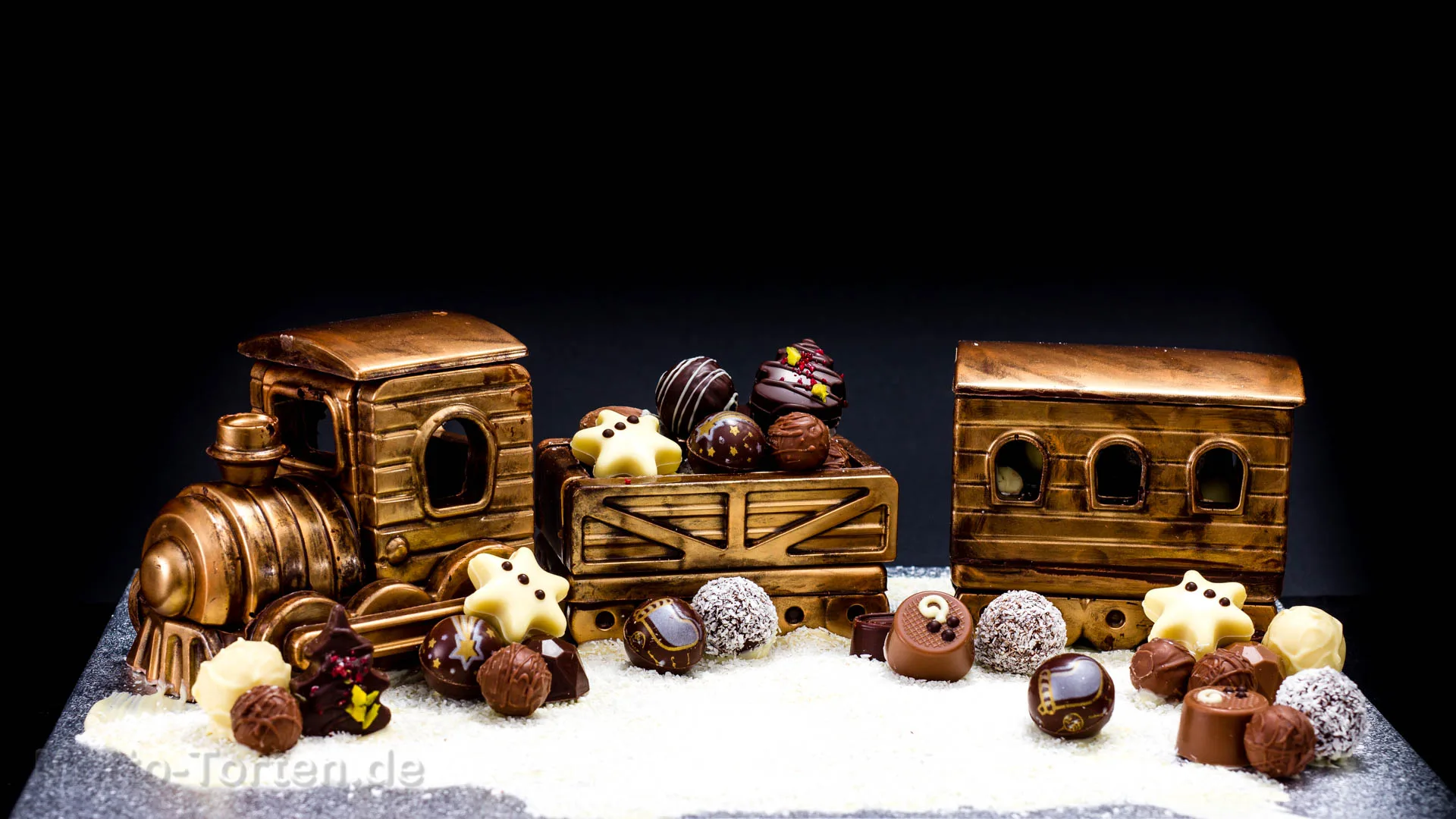 Weihnachtliche Pralinenmischung in verschiedenen Sorten, daneben eine aus Schokolade gegossene Eisenbahn mit Bronzefarbe