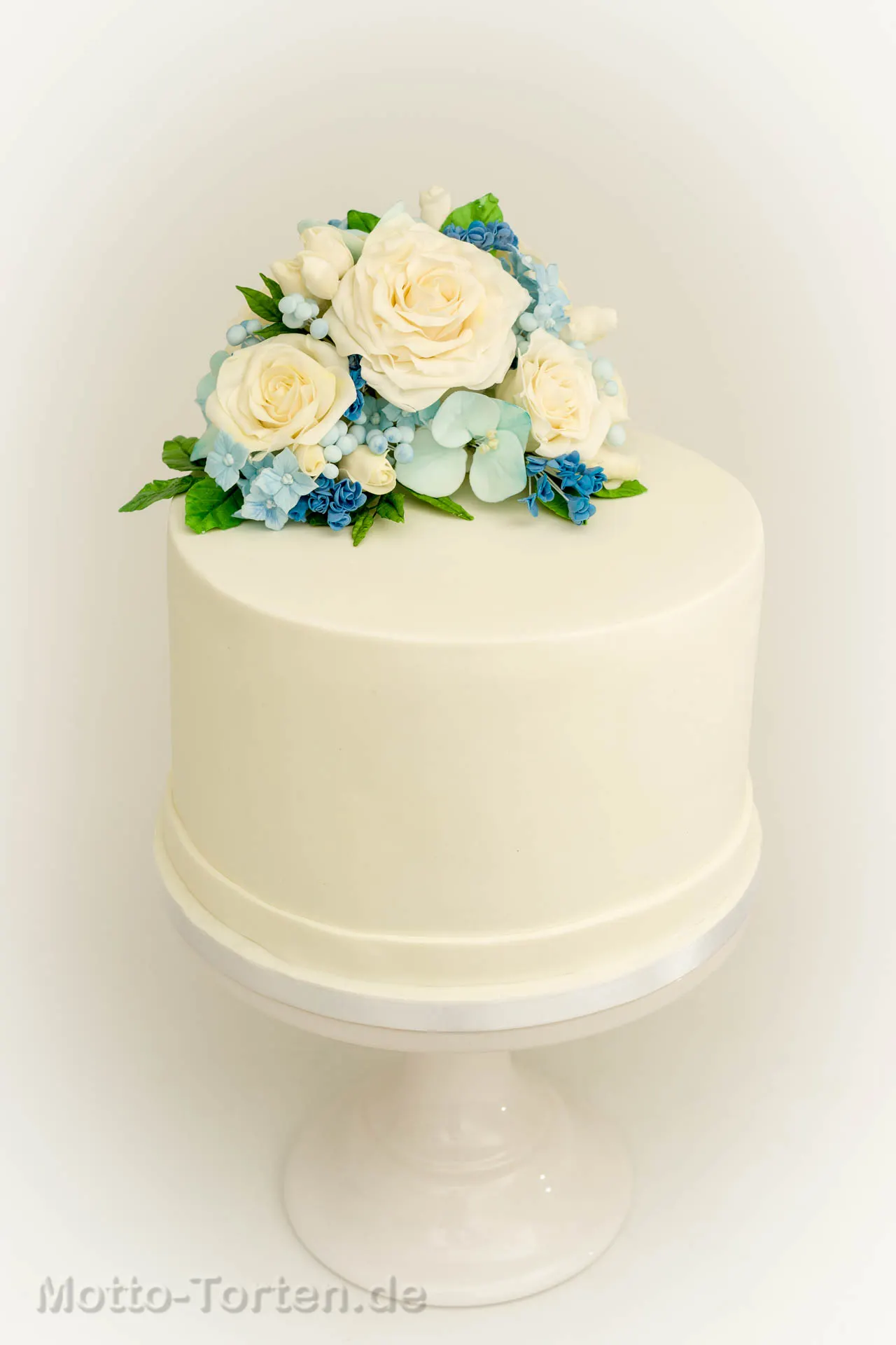 Nahaufnahme des Bouquets auf der Hochzeitstorte: cremeweiße Rosen aus Blütenpaste mit hellblauen Füllblümchen, Beeren und Eukalyptusblättern – Ansicht 2