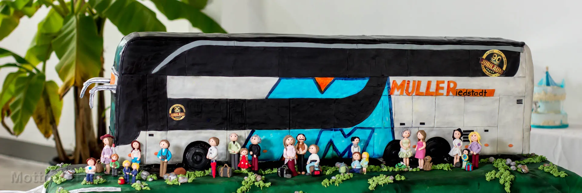 Anderthalb Meter lange Torte als Setra-Doppeldeckerbus mit Müller-Schriftzug, davor eine Reisegesellschaft aus handmodellierten Fondantfiguren mit Gepäck – Ansicht 2