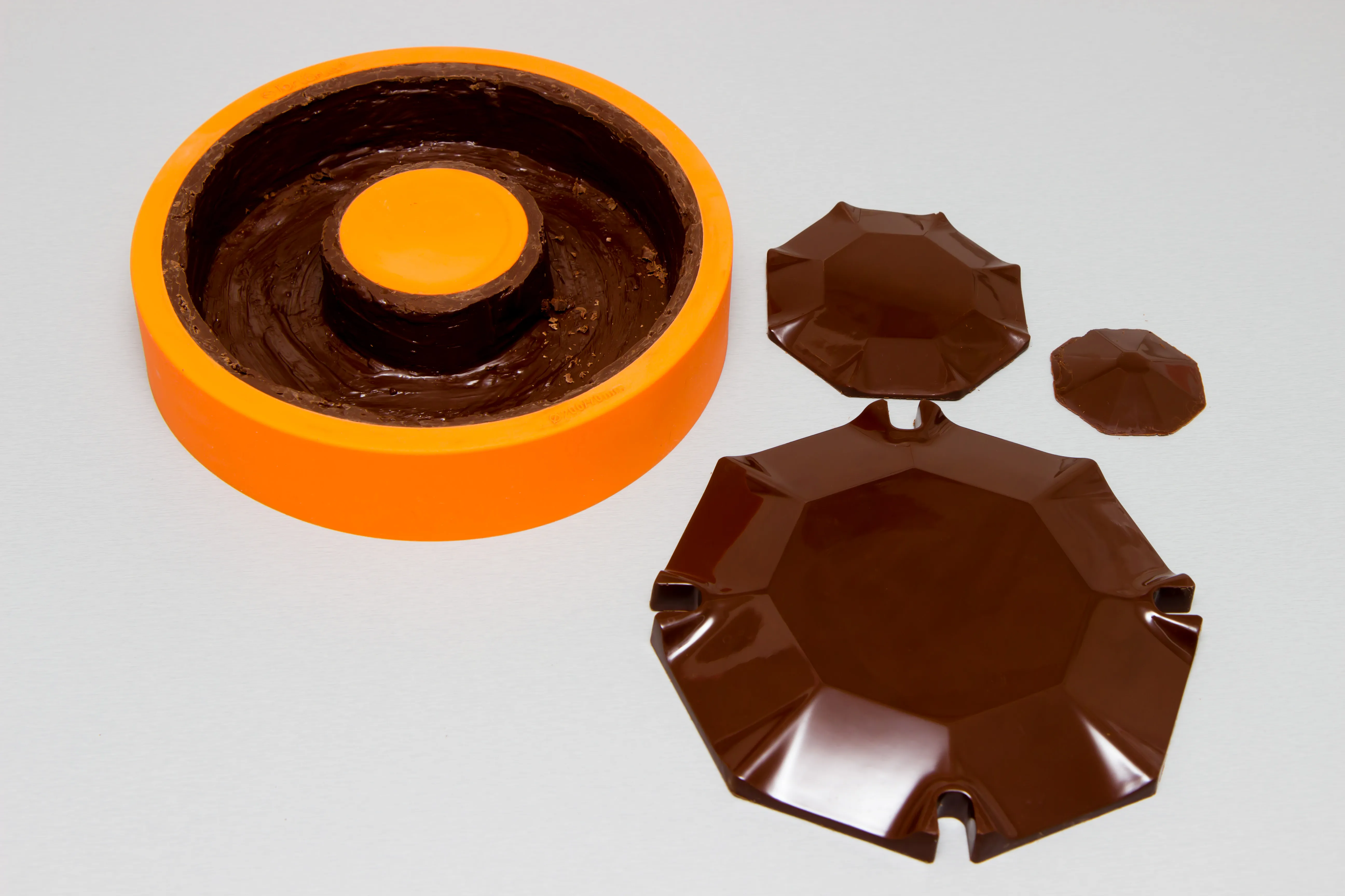 Die orange Silikonform mit der eingepinselten Grundform, daneben Dach und Deckel aus Schokolade