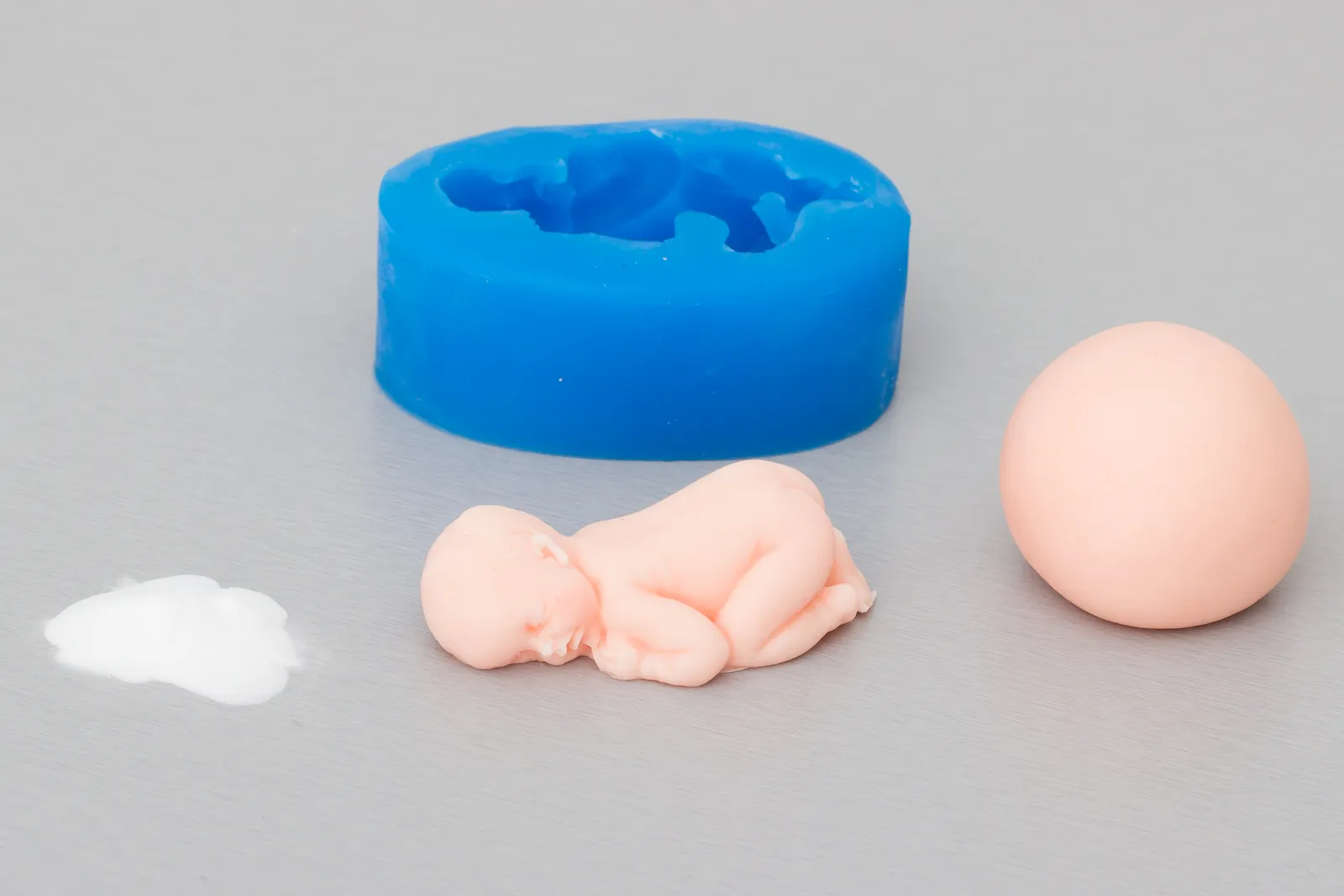 Blaue Silikonform, eine Kugel hautfarbener Fondant, Bäckerstärke und ein ausgeformtes Baby