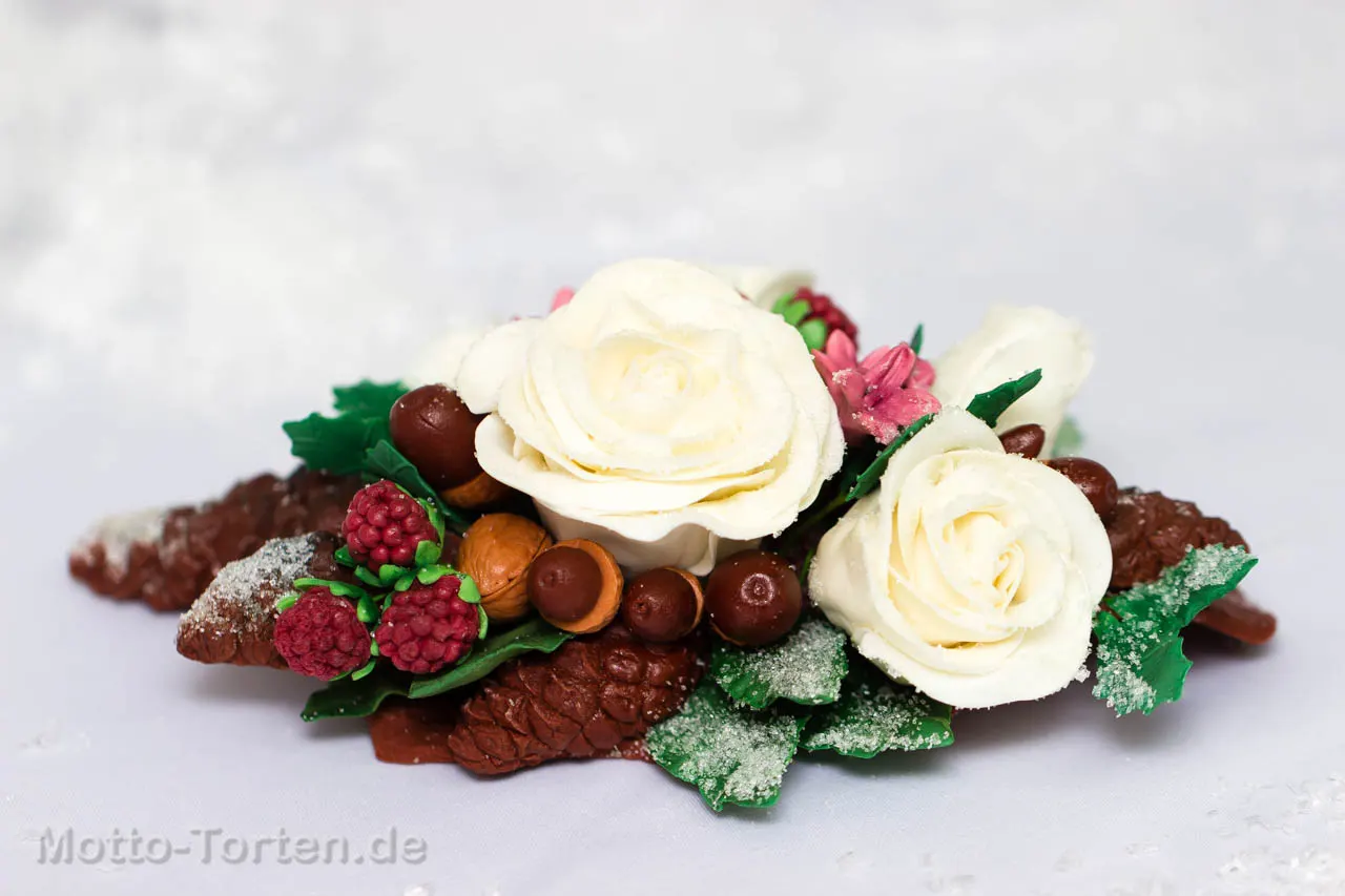 Zweistöckige Hochzeitstorte mit weißer Buttercreme und dunkelrotem Fondantband, darauf ein Wintergesteck aus Rosen, Tannenzapfen, Nüssen und Beeren mit Zuckerreif – Ansicht 2