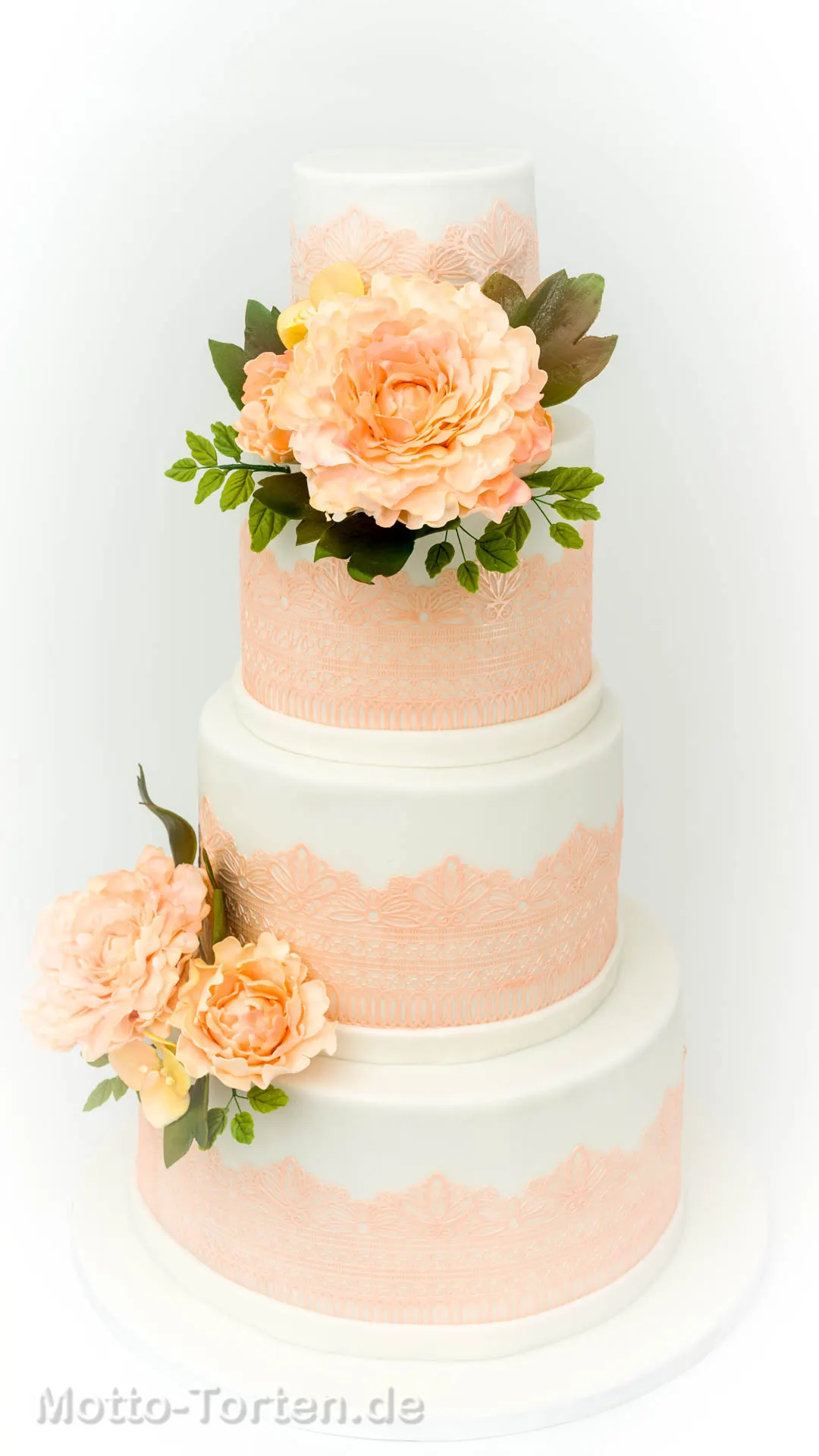 Mehrstöckige weiße Hochzeitstorte mit apricotfarbener essbarer Spitze und handmodellierten Pfingstrosen in Apricot mit grünen Blättern – Ansicht 3