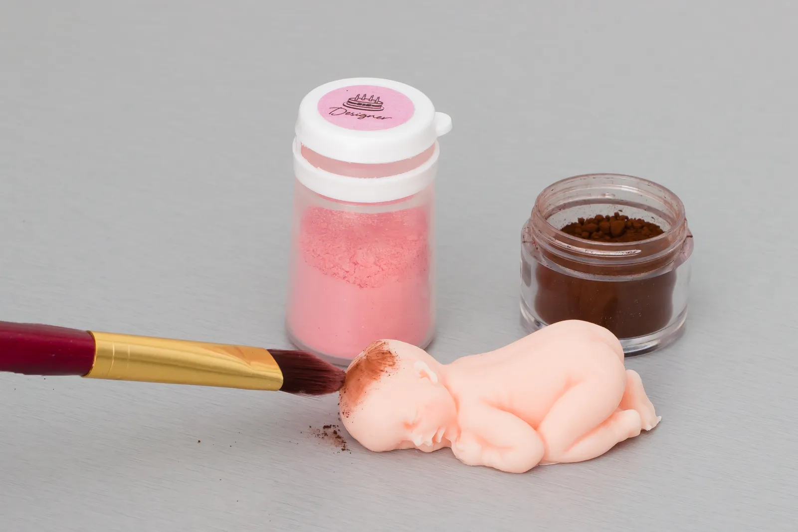 Rosa und braune Pulverfarbe mit Pinsel neben dem ausgeformten Baby