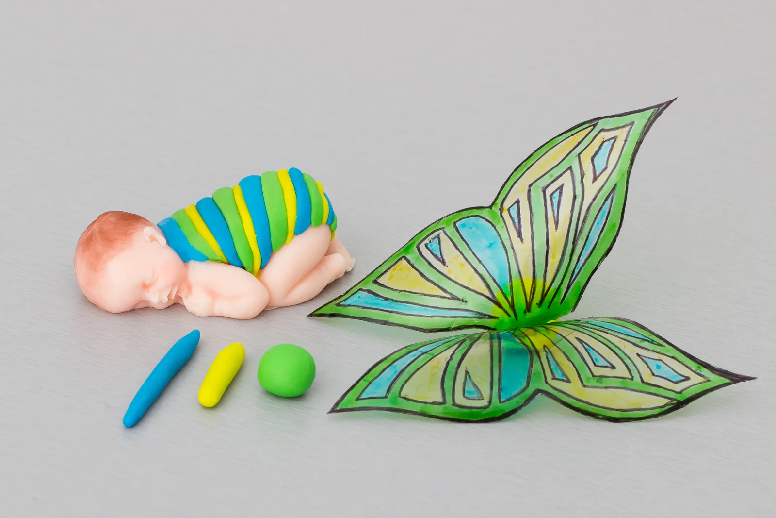 Das Baby mit gestreiftem Fondantkörper, daneben die fertigen Flügel