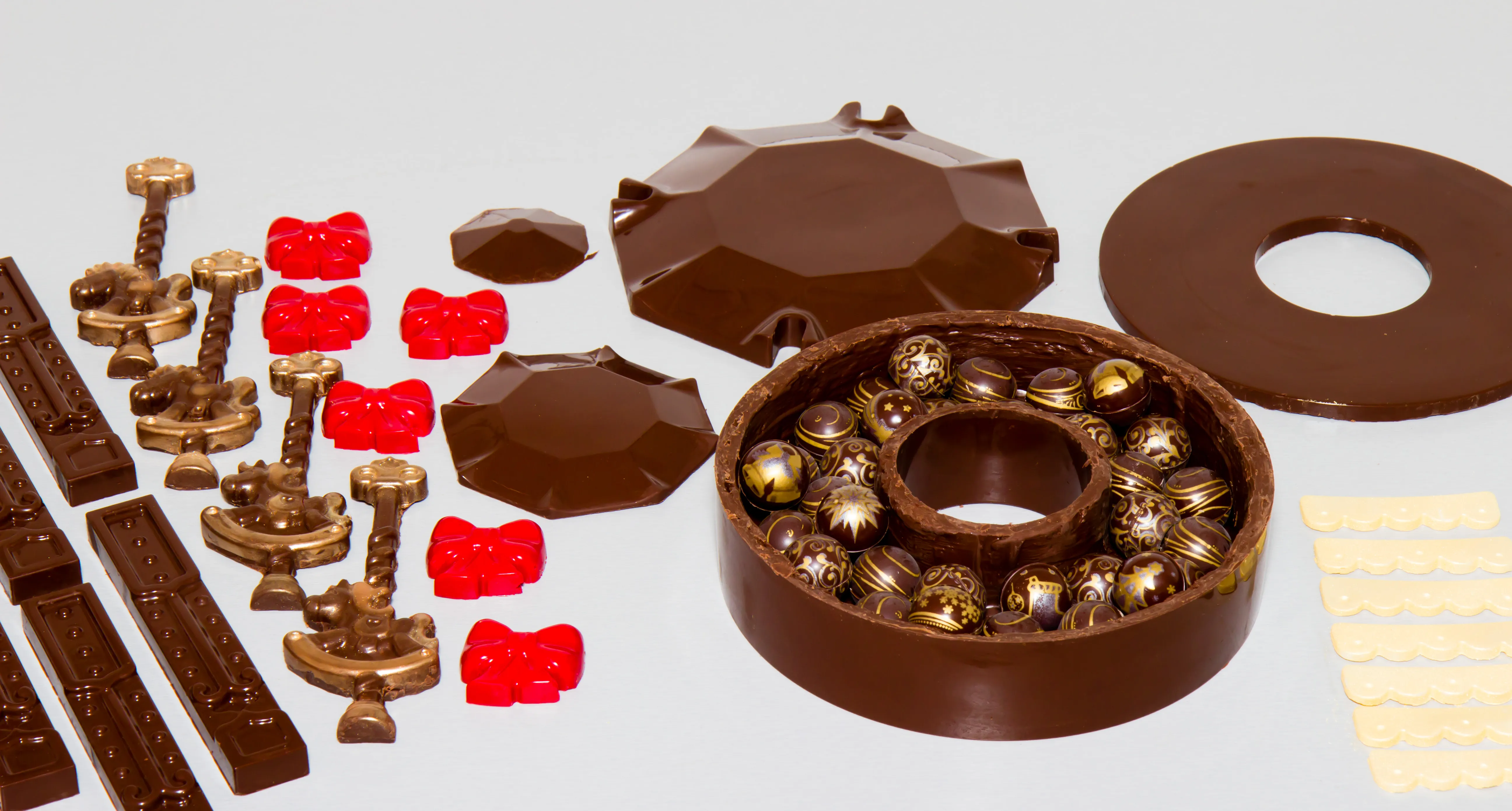 Alle vorbereiteten Schokoladenteile nebeneinander, die Grundform ist mit Pralinen gefüllt