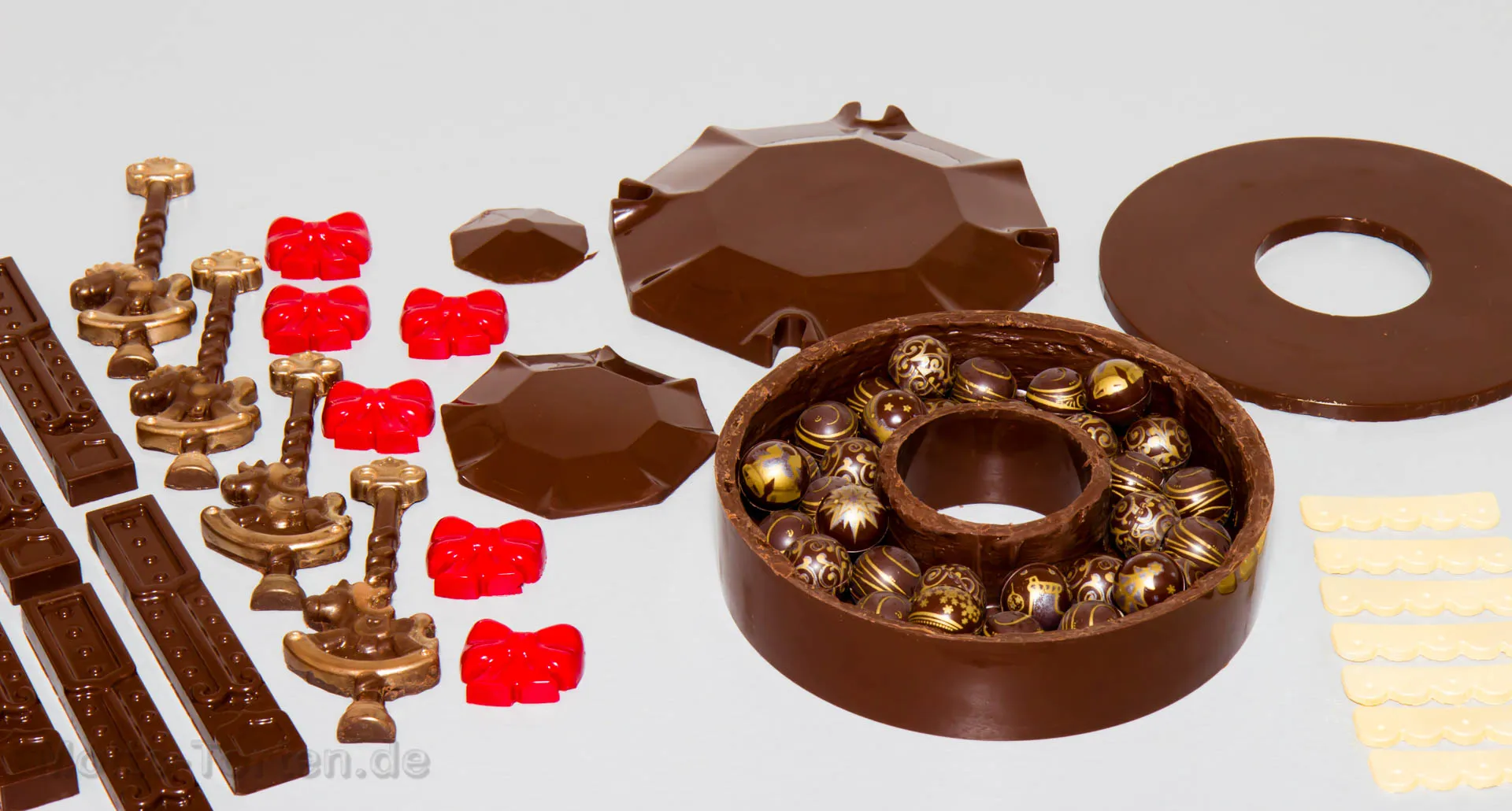 Alle vorbereiteten Schokoladenteile nebeneinander, die Grundform ist mit Pralinen gefüllt